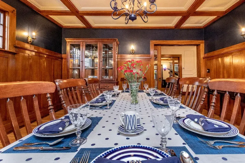 A dining room table with plates , utensils , and a vase of flowers on it.
