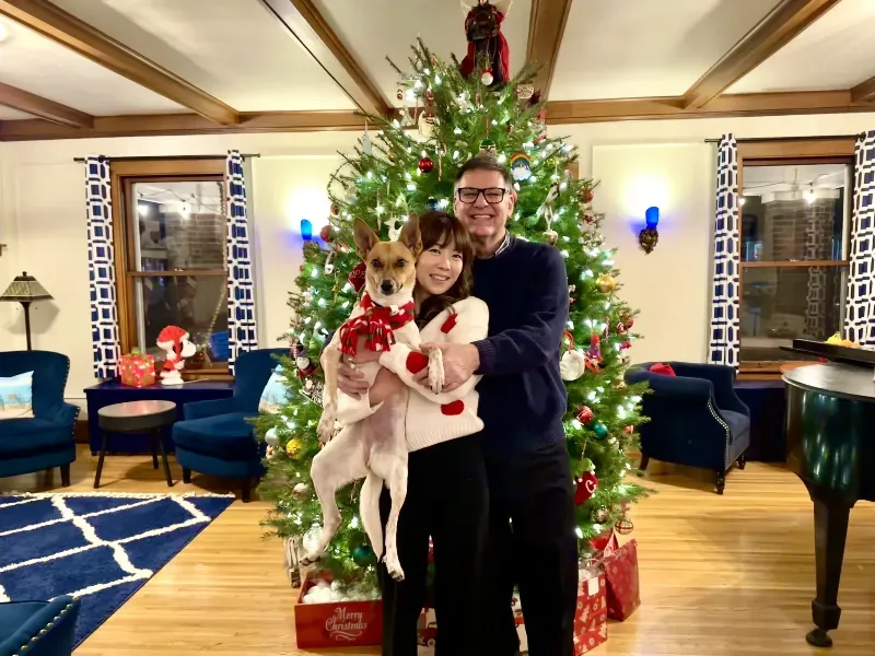 A man and woman are holding a dog in front of a christmas tree.