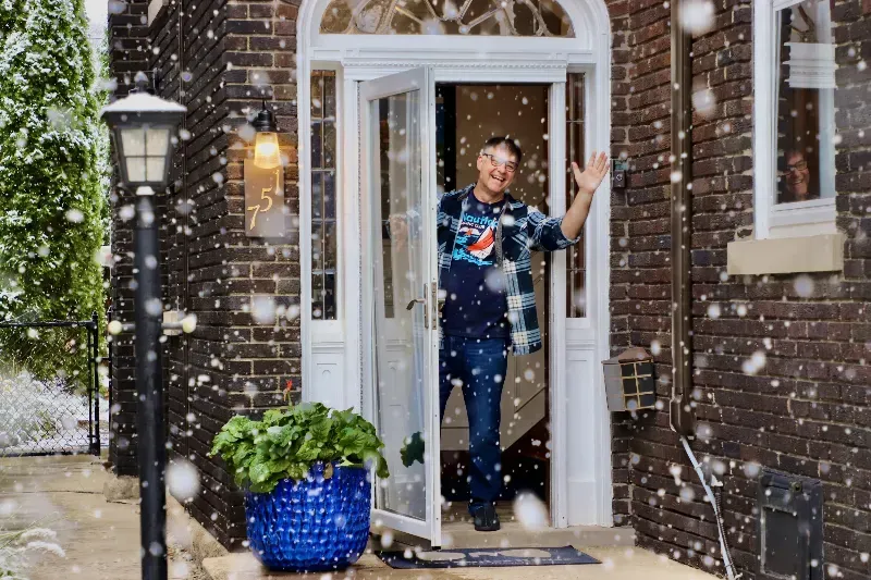 A man is standing in the doorway of a house in the snow.