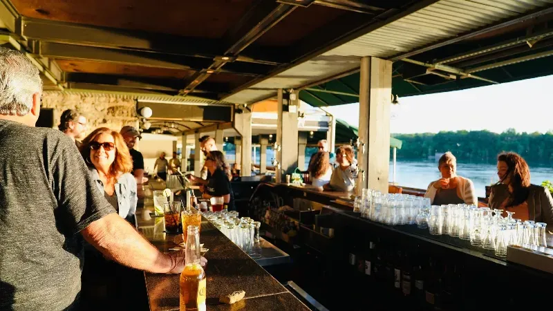 A group of people are sitting at a bar with a view of a lake.