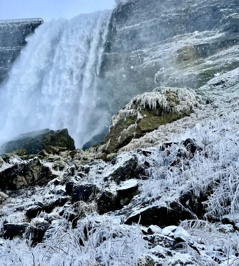A waterfall is surrounded by snow covered rocks and grass