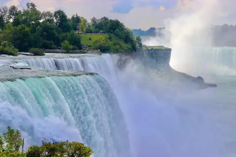 A waterfall is surrounded by trees and a body of water.