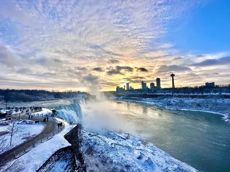 A view of niagara falls in the winter with a sunset in the background.