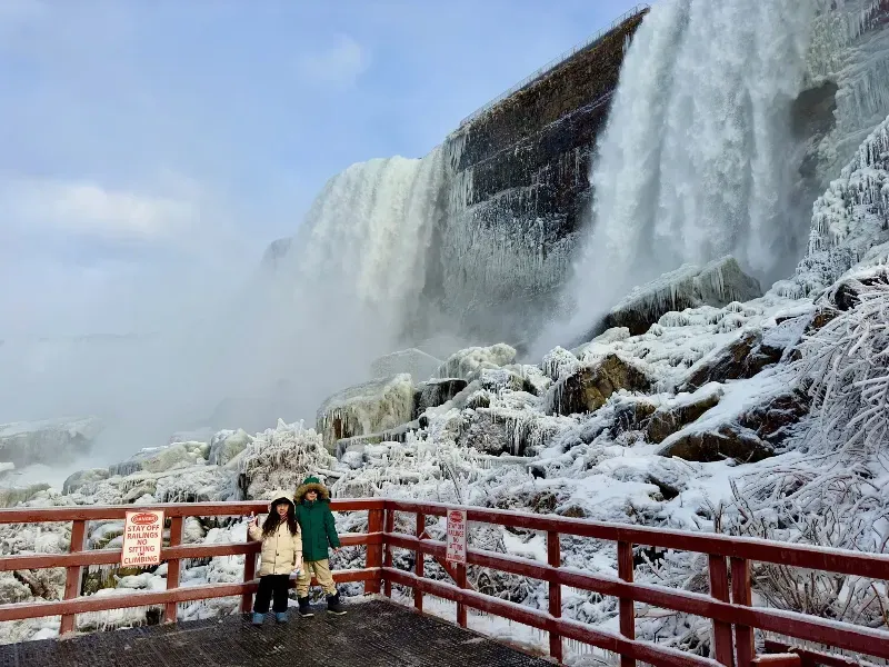 Two people are standing in front of a waterfall covered in snow.