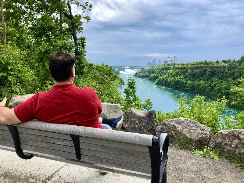A man is sitting on a bench overlooking a river.