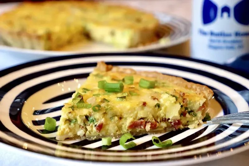 A slice of quiche is on a striped plate with a fork.
