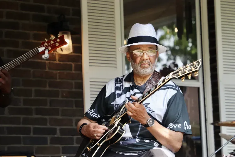 A man in a hat is playing a guitar on a porch