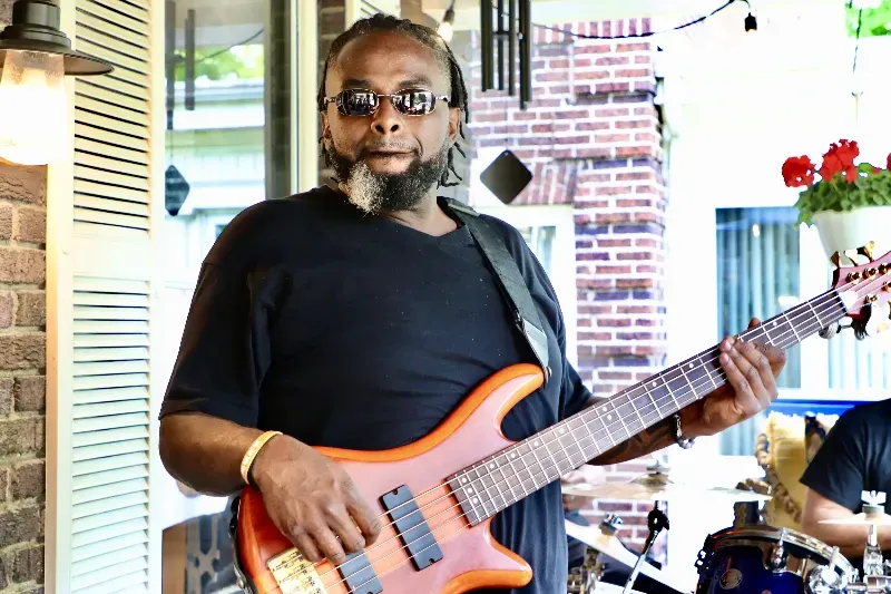 A man is playing a guitar in front of a brick wall.