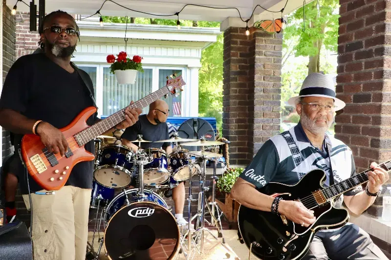 Two men are playing guitars and drums on a porch.