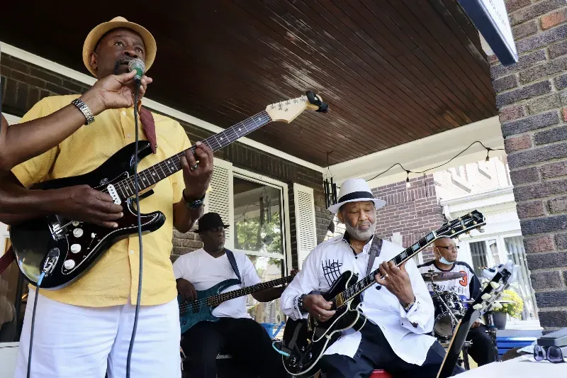A group of men are playing guitars and singing into microphones on a porch.