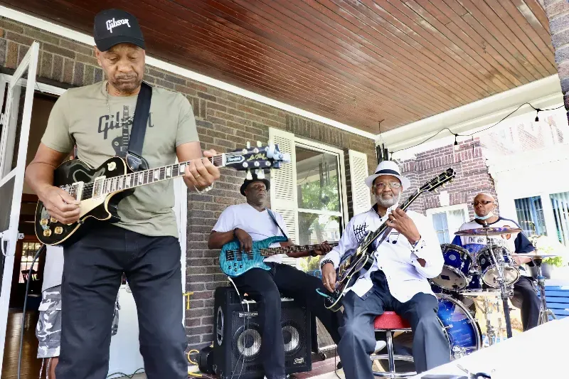 A group of men are playing guitars and drums on a porch.
