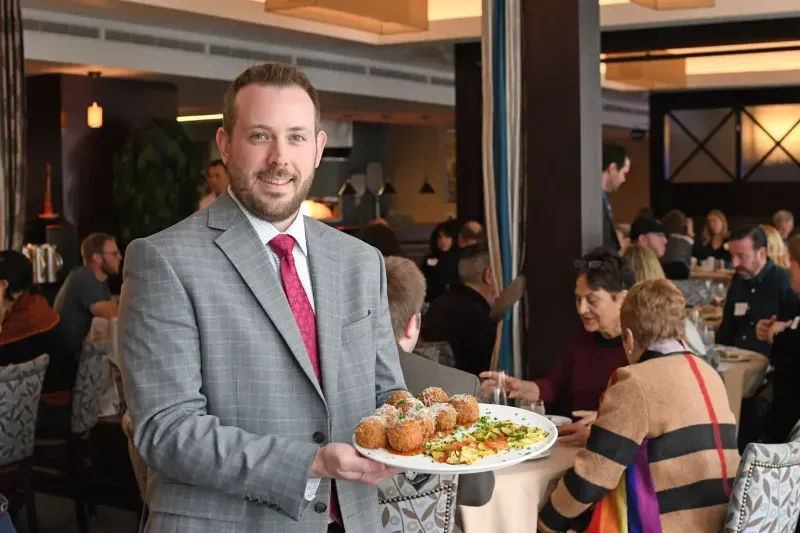 A man in a suit and tie is holding a plate of food in a restaurant.