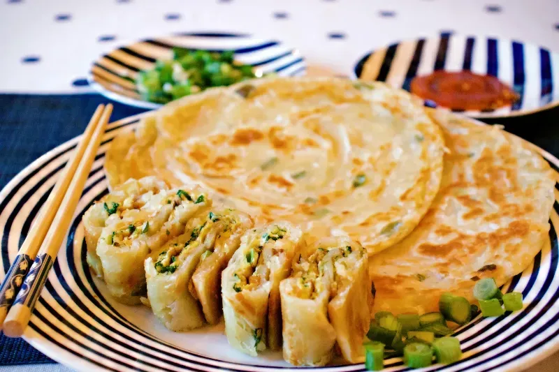 A plate of food with chopsticks and green onions on a table.
