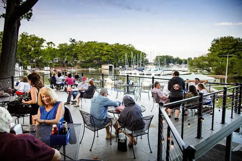 A group of people are sitting at tables on a deck overlooking a body of water.