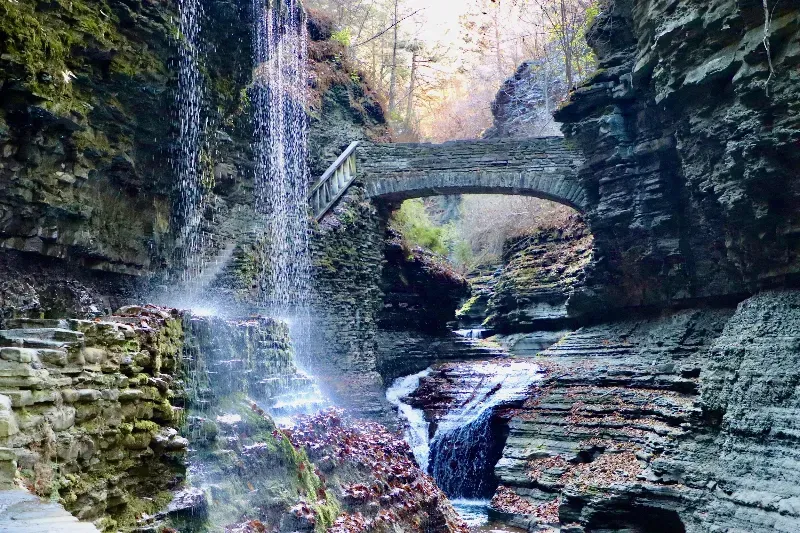 A waterfall in a canyon with a bridge in the background.
