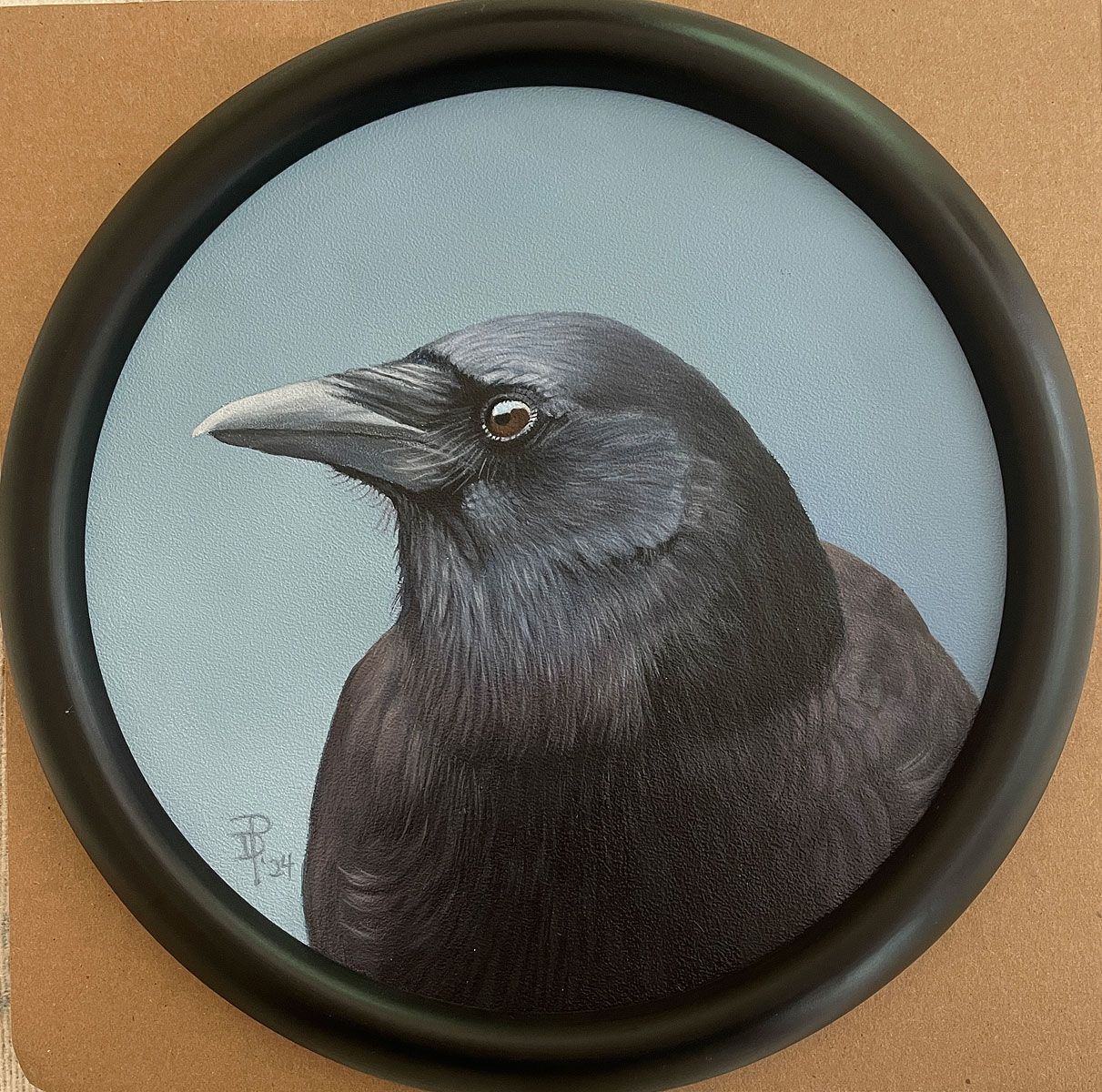 A realistic, circular painting of a crow against a soft blue background, framed in a simple black circular frame.