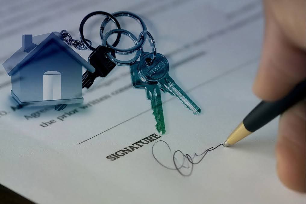 Person signing a real estate contract with a graphic of home keys overlayed