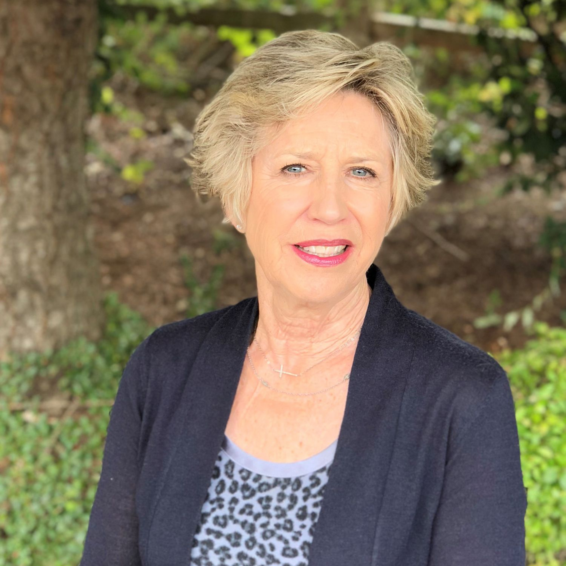 Woman with short blonde hair and a dark cardigan smiling outdoors.
