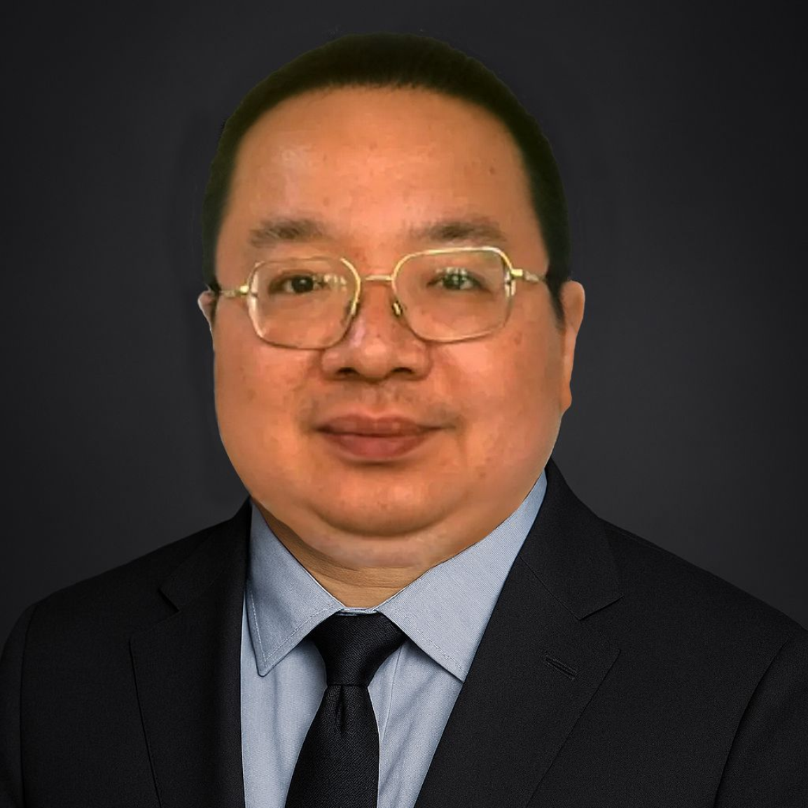 Man in suit, glasses, and tie against a dark background, looking forward.