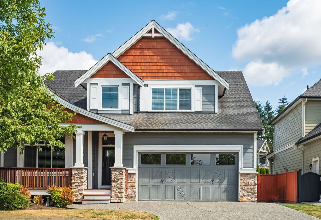 Suburban house with gray roof, red wood gable, white trim, and a two-car garage under a blue sky