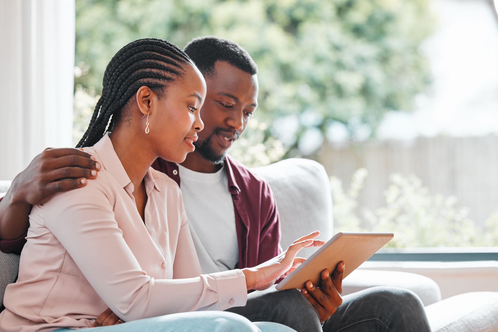Two people sitting on a couch, smiling and looking at a tablet together in a bright living room