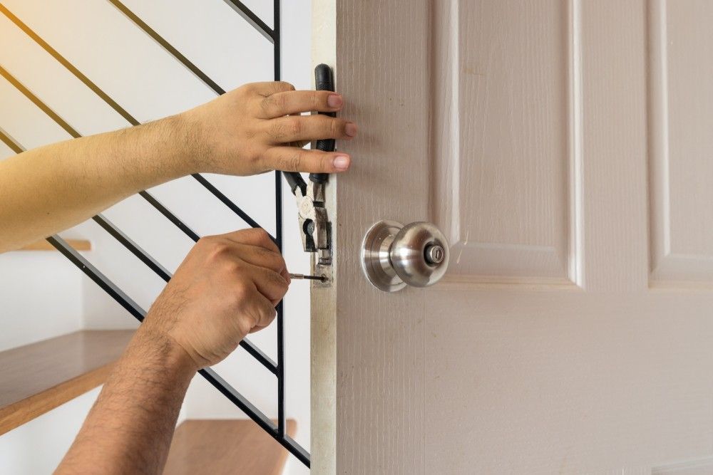A Man is Fixing a Door With a Screwdriver — Suresafe Locksmiths in Glenvale, QLD