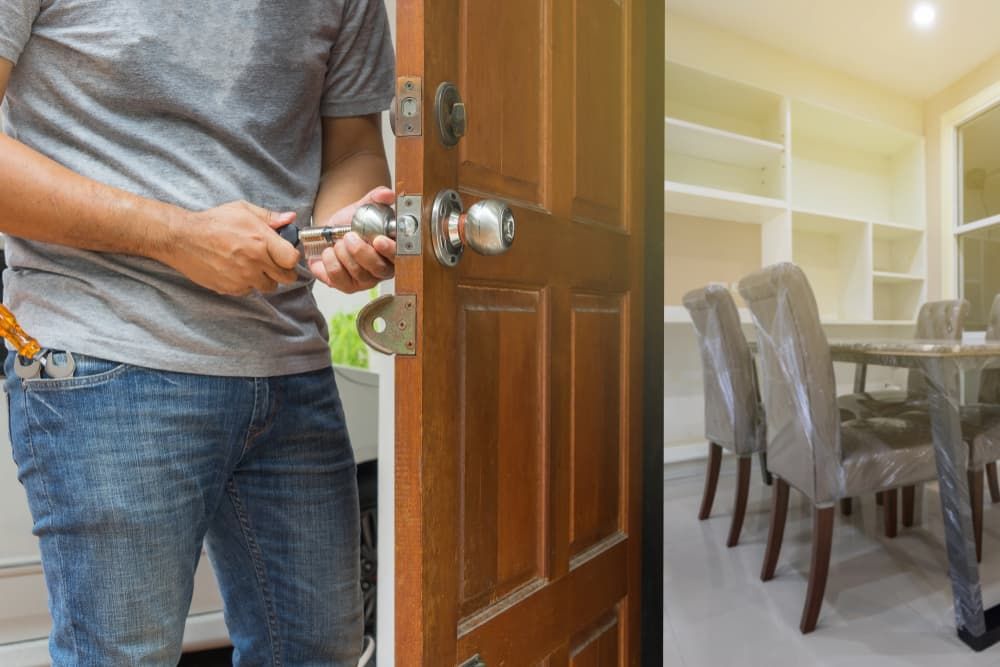 A Person in a Gray Shirt and Jeans Uses a Screwdriver on a Wooden Door Lock