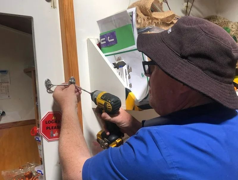A Man in a Hat is Using a Drill to Fix a Door — Suresafe Locksmiths in Glenvale, QLD