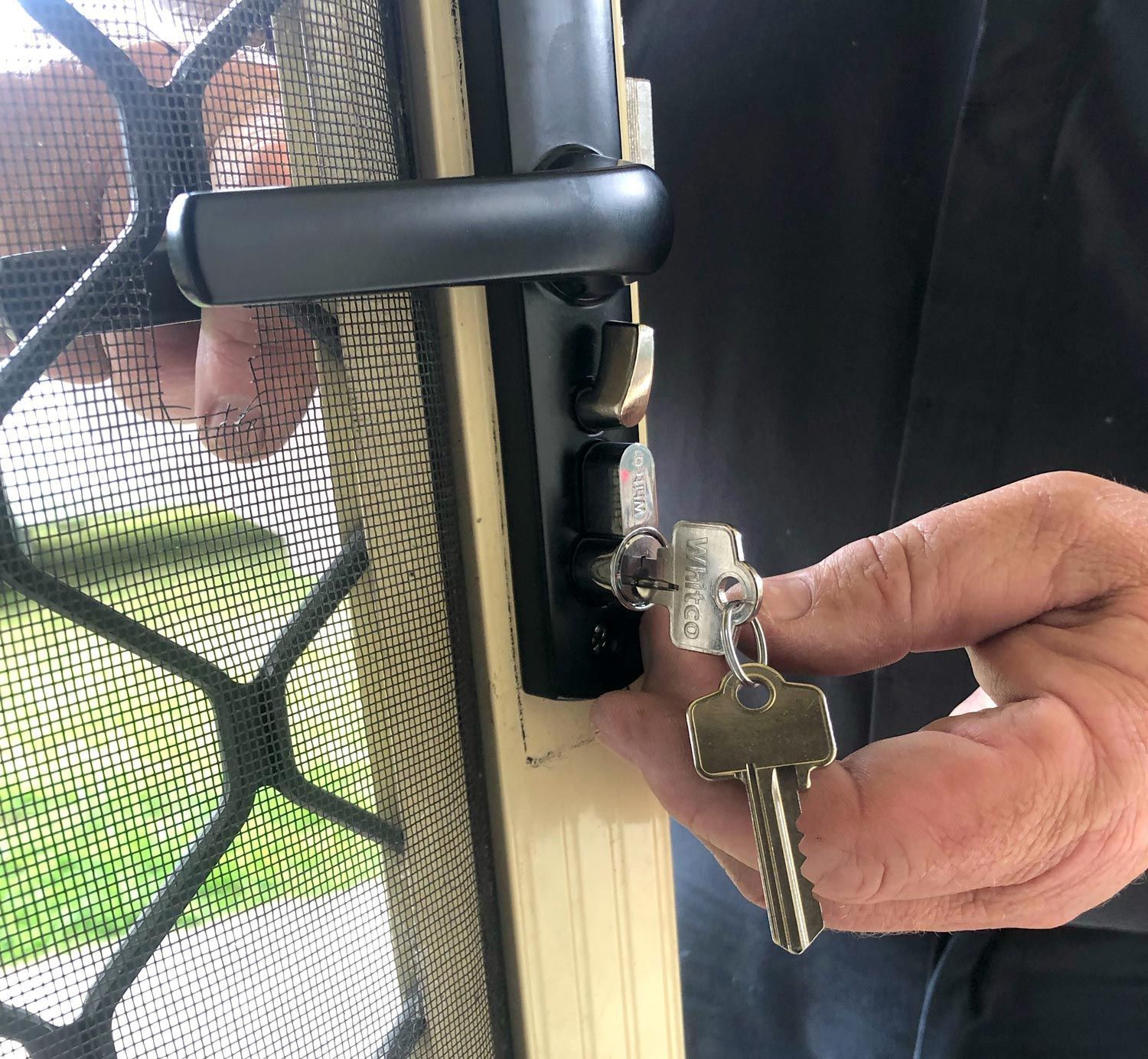 A Person is Holding a Key in Front of a Screen Door — Suresafe Locksmiths in Glenvale, QLD