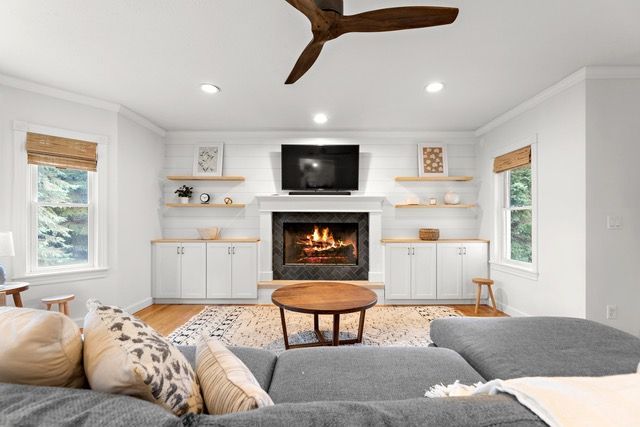Living room with fireplace, white walls, wooden shelves, a gray sectional, and a coffee table.