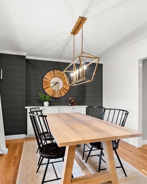 Dining room with wooden table, black chairs, and gold chandelier against a black accent wall.