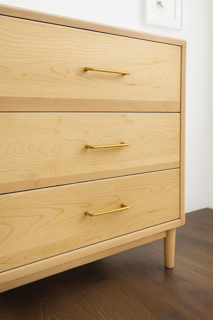Light wood dresser with three drawers, gold handles, and round legs.