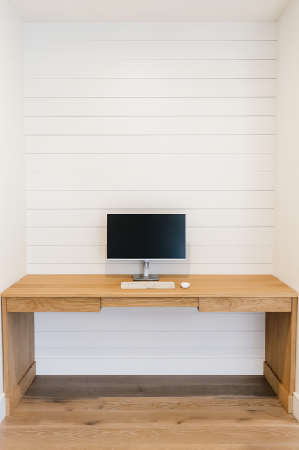 Wooden desk with computer, keyboard, and mouse against a white shiplap wall.