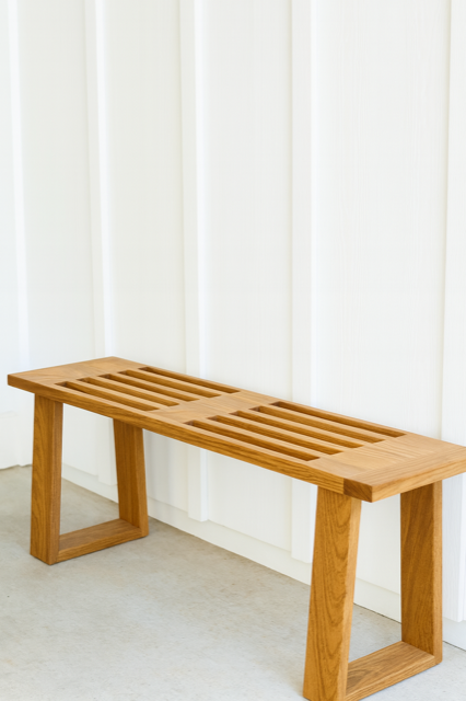 Wooden bench with slatted seat against a white paneled wall.