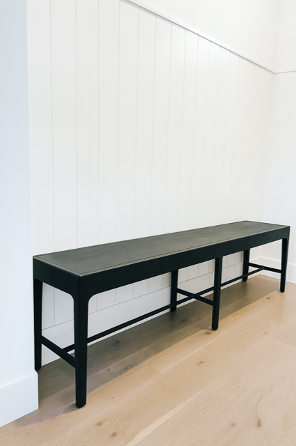 Black bench against white paneled wall on wood floor.