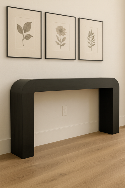 Black console table with rounded edges below three framed botanical prints on a white wall.