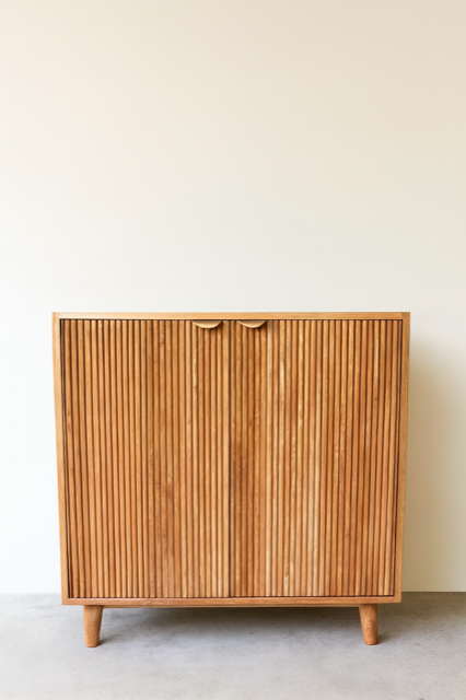 Wooden cabinet with ribbed doors and small handles against a cream wall and grey floor.