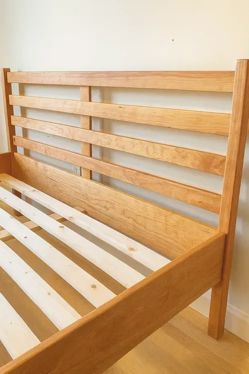 Wooden bed frame with a slatted headboard, light brown stain, and a wooden slat foundation.