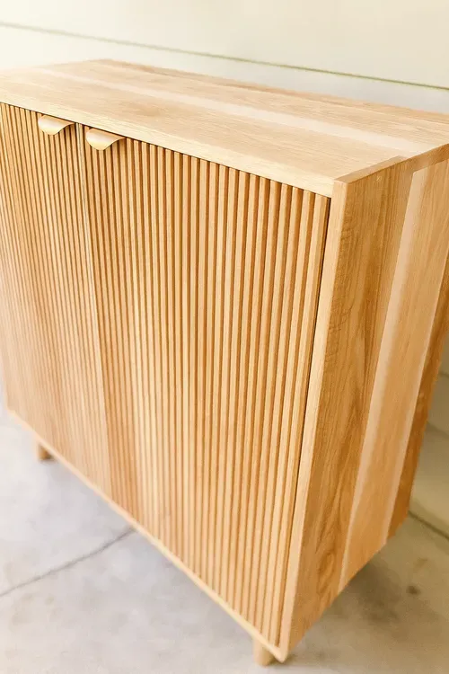 Wooden cabinet with vertical ridged door detail and small rounded handles.
