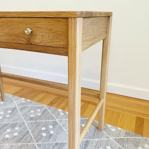 Wooden desk with a drawer and gold knob, set on a geometric patterned rug.