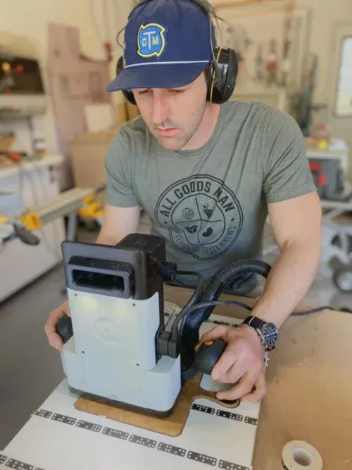 Man using a sanding tool, wearing safety gear in a workshop.