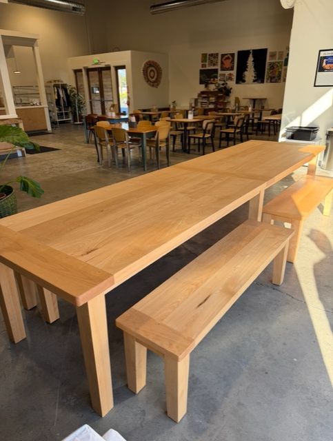 Wooden table and bench in a brightly lit room with more tables and chairs in the background.