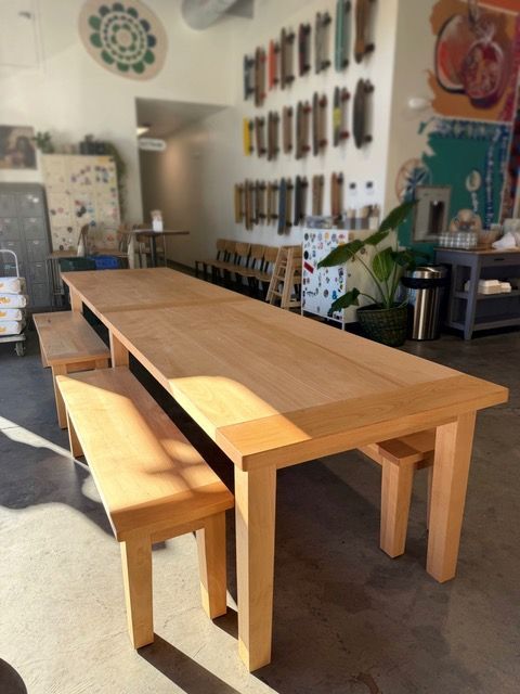 Wooden table with benches in a brightly lit cafe setting; artwork on the wall.