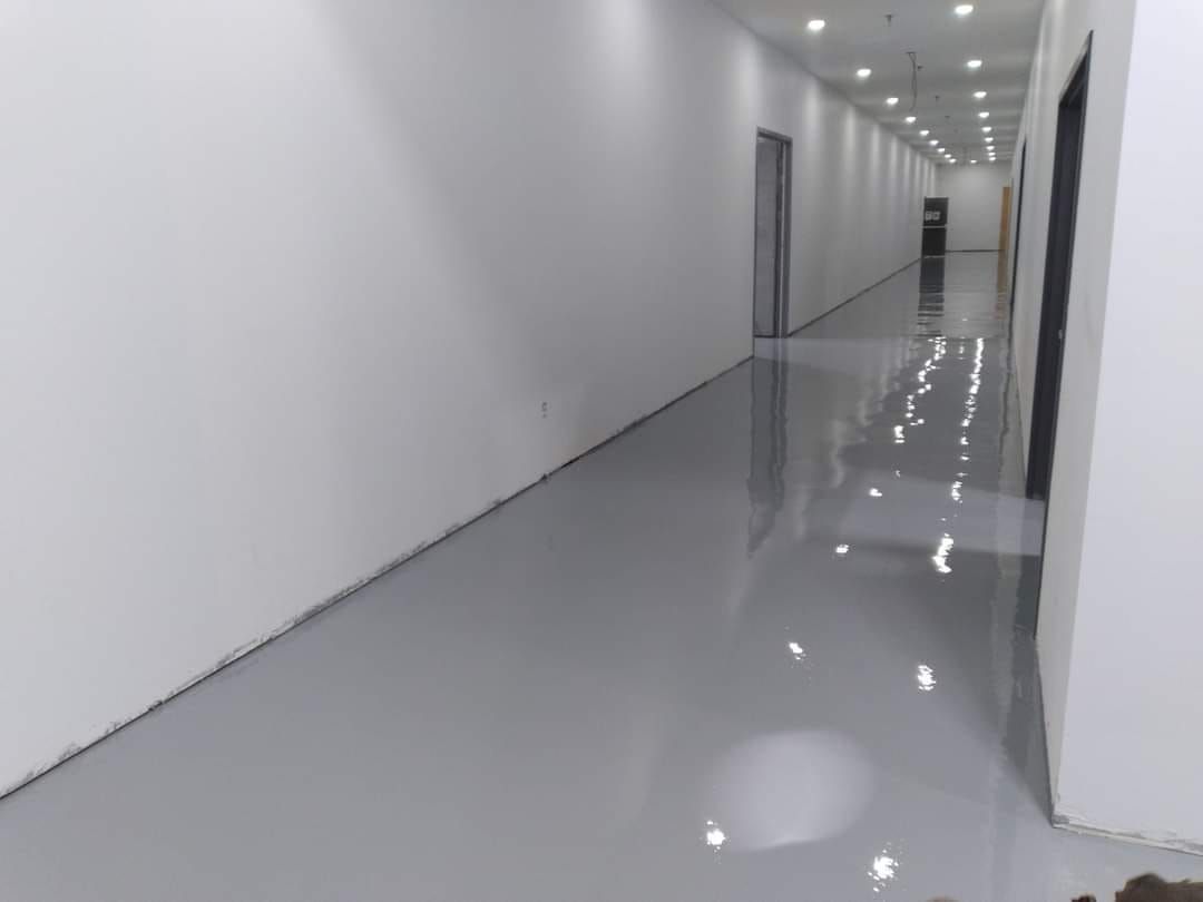 Un long couloir avec un sol gris et des murs blancs.