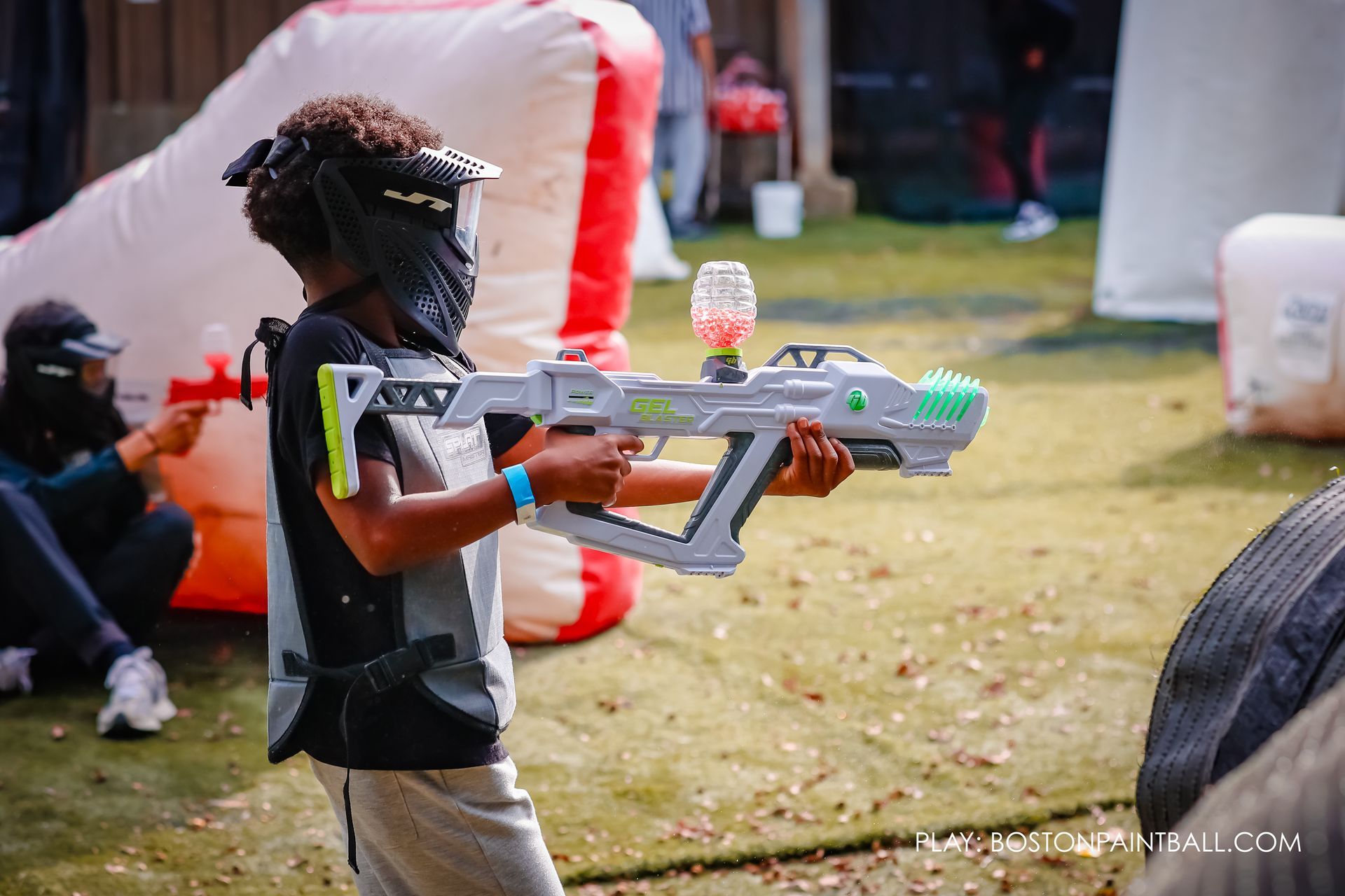 Child playing GellyBall at Boston Paintball, wearing safety gear and holding a GellyBall blaster on the outdoor field.