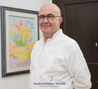 Uomo in camicia bianca e occhiali, sorridente, vicino a un dipinto floreale incorniciato. È visibile il logo 