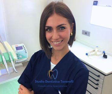 Dentista sorridente in camice blu, braccia incrociate. Studio con attrezzature odontoiatriche. Logo dello Studio Dentistico Tencrelli.
