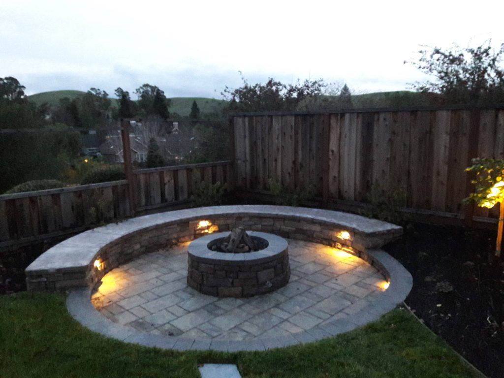 A fire pit is surrounded by a wooden fence and is lit up at night.