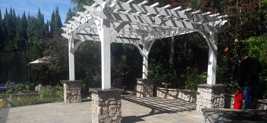 A white pergola is sitting on top of a stone patio.