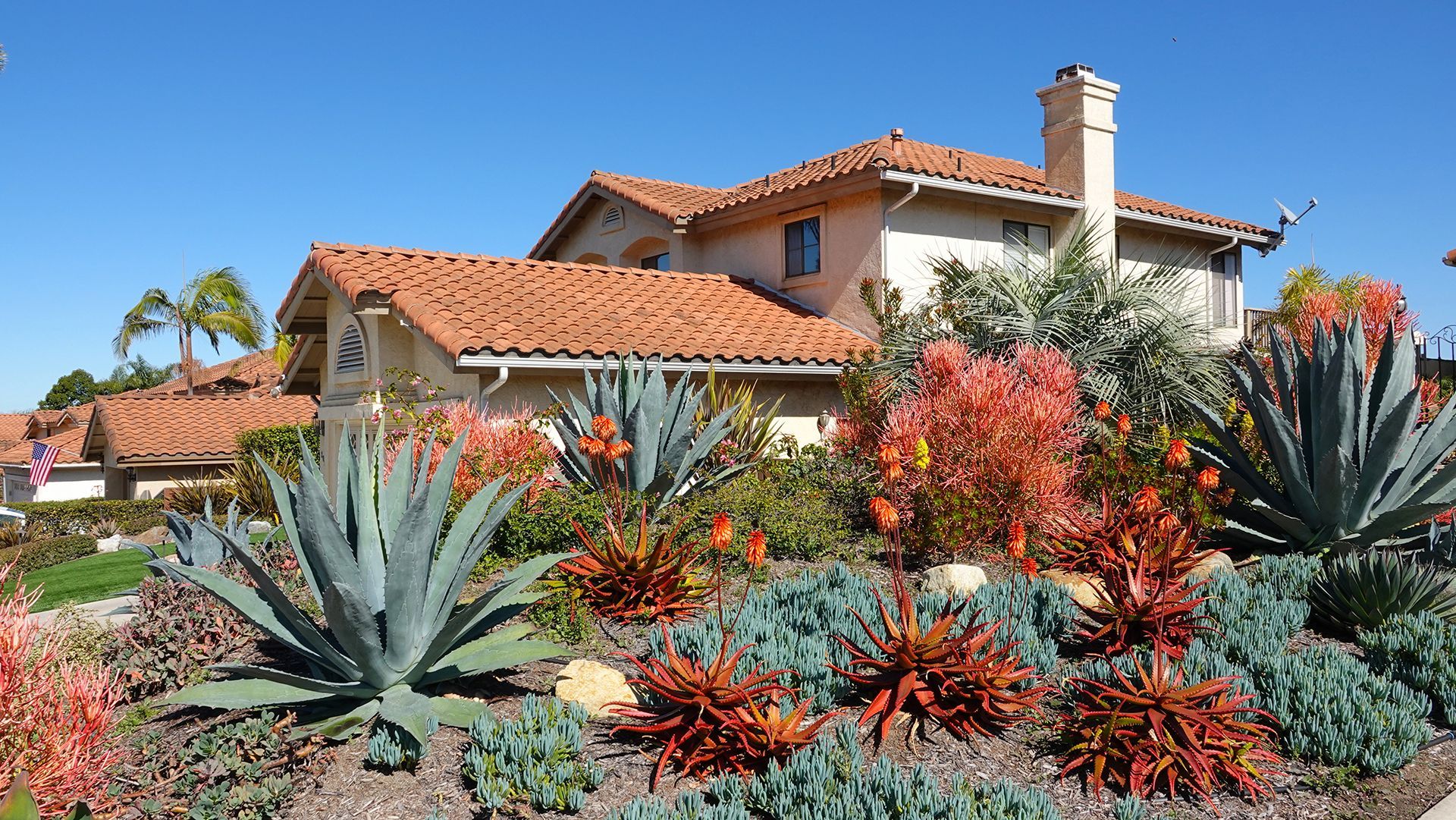 A large house with a red tile roof is surrounded by a lush green garden.